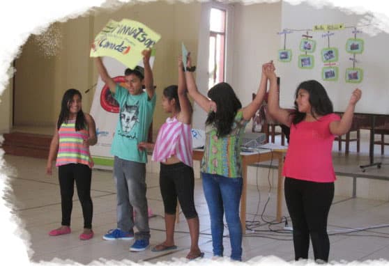 Group of children displaying their hands painted with yellow paint, standing proudly in front of a mural that emphasizes community involvement and youth empowerment.